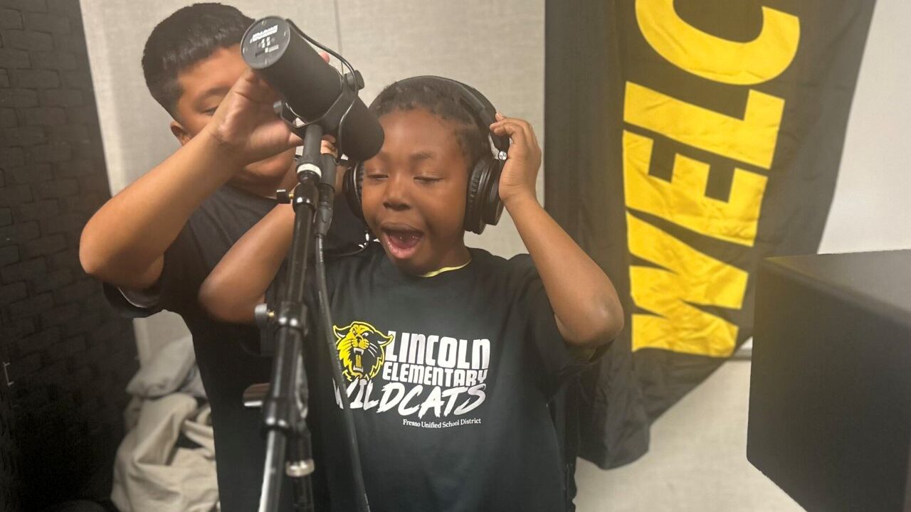 Image of a Black student with headphones over his ears singing into a microphone