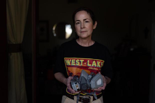 Nina Malone, whose home survived the Eaton Fire, stands for a photo with a respirator she uses when cleaning fire debris inside her home, Dec. 11, 2025, in Altadena, Calif. (AP Photo/Jae C. Hong)