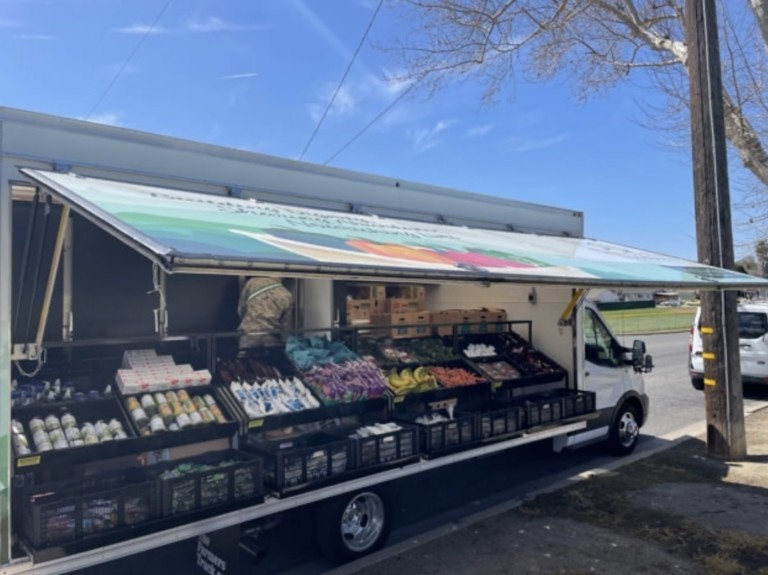 A food truck with an open side displaying fresh produce and groceries.