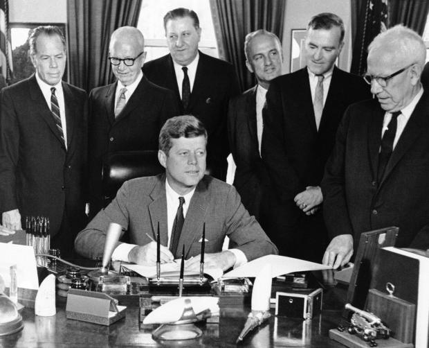President John Kennedy has pen in hand as he sign the $4,672,000,000 foreign aid authorization bill in his White House office in Washington August 1, 1962. A large bipartisan congressional delegation was on hand for the ceremony. In the background, from left, are; Sen. Thomas Kuchel, R-Calif., Rep. Francis E. Walter, D-Pa., Rep. Thomas E. Morgan, D-Pa., Rep. Peter Frelinghuysen, R-N.J., Rep. Cornelius E. Gallagher, D.-N.J., and Sen. George D. Aiken, R-Vt. (AP Photo/John Rous)