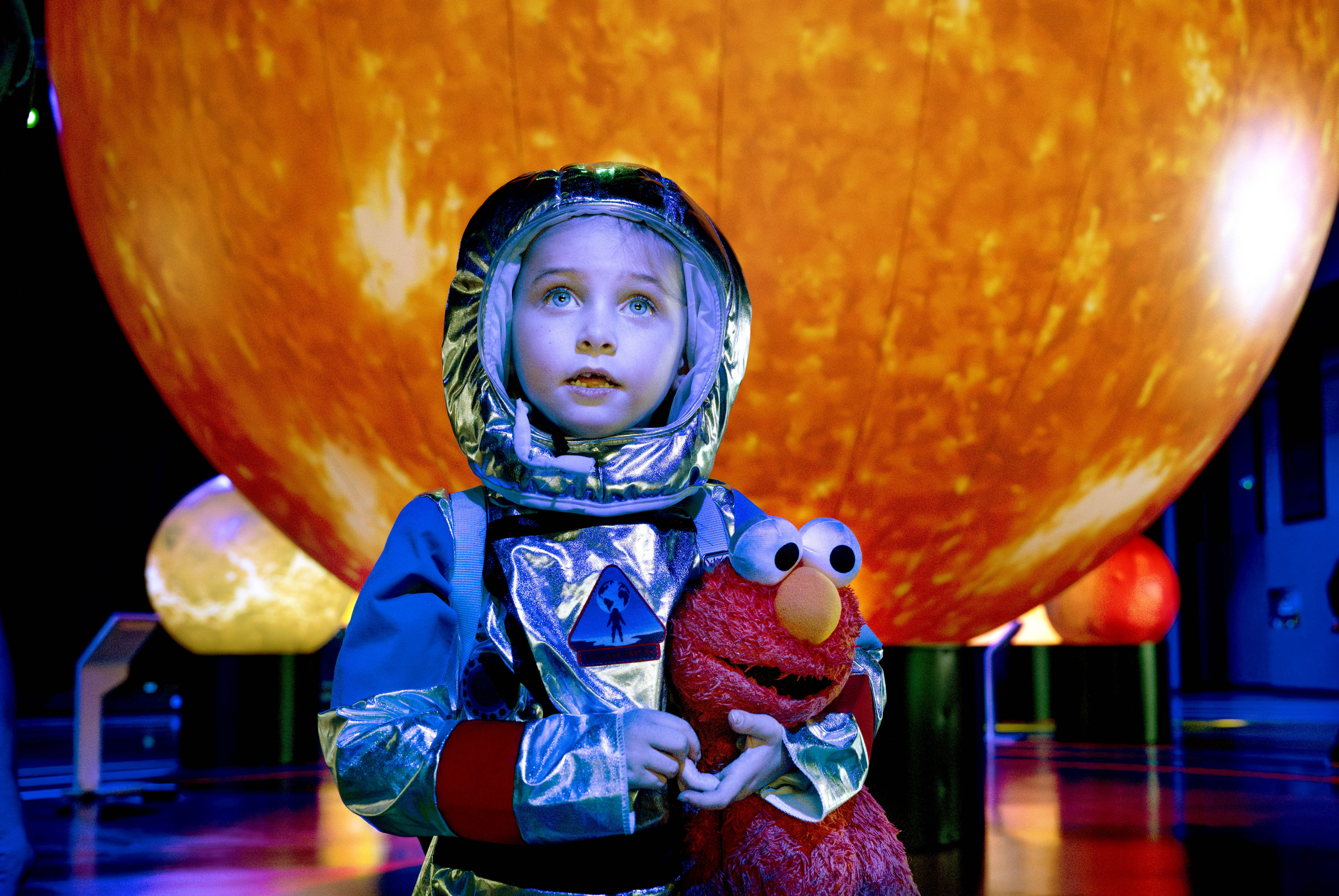 Dressed like an astronaut and holding her stuffed Elmo doll,...