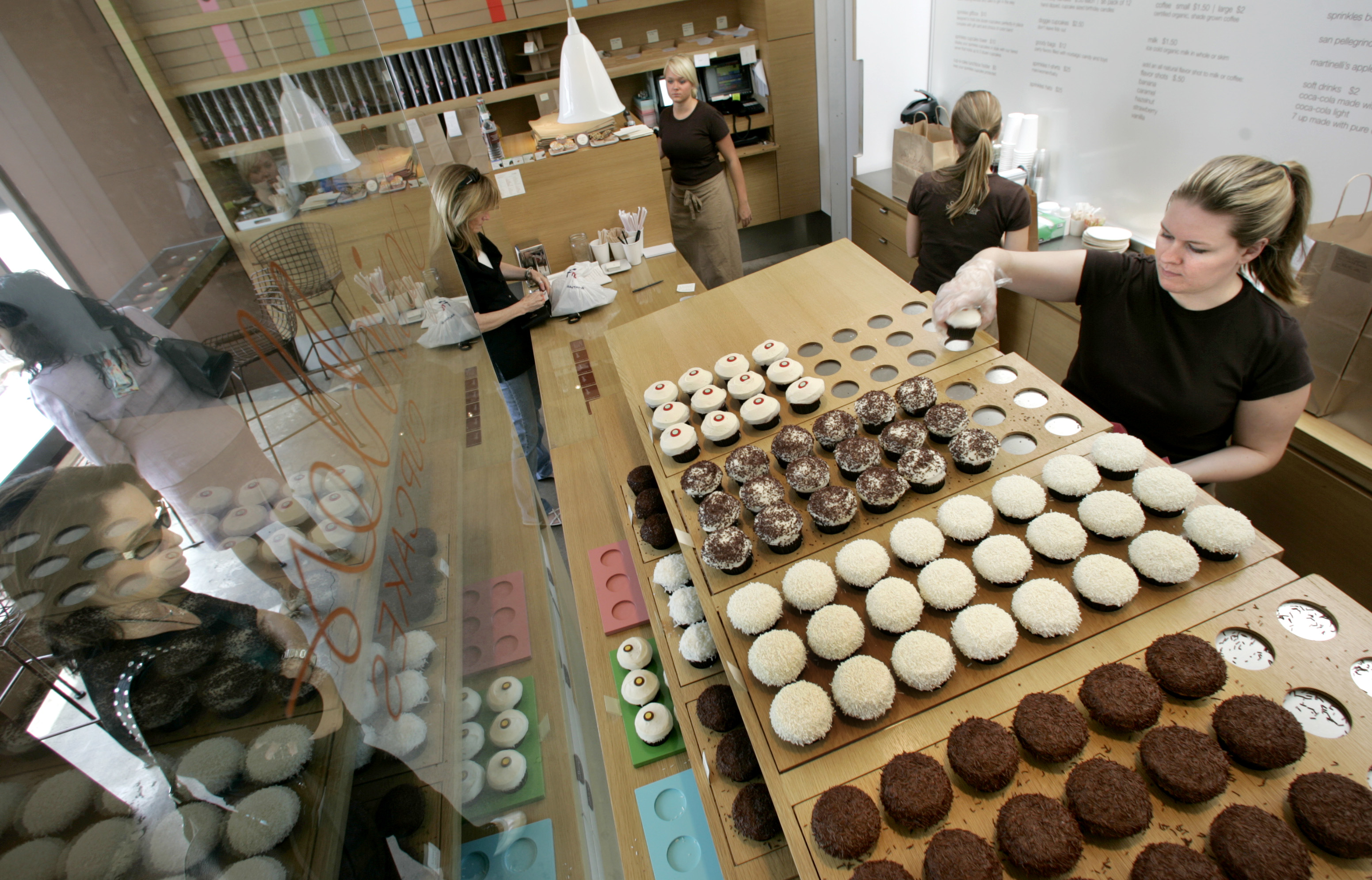 A customer watches as a “cupcake associate” serves Sprinkles Cupcakes...