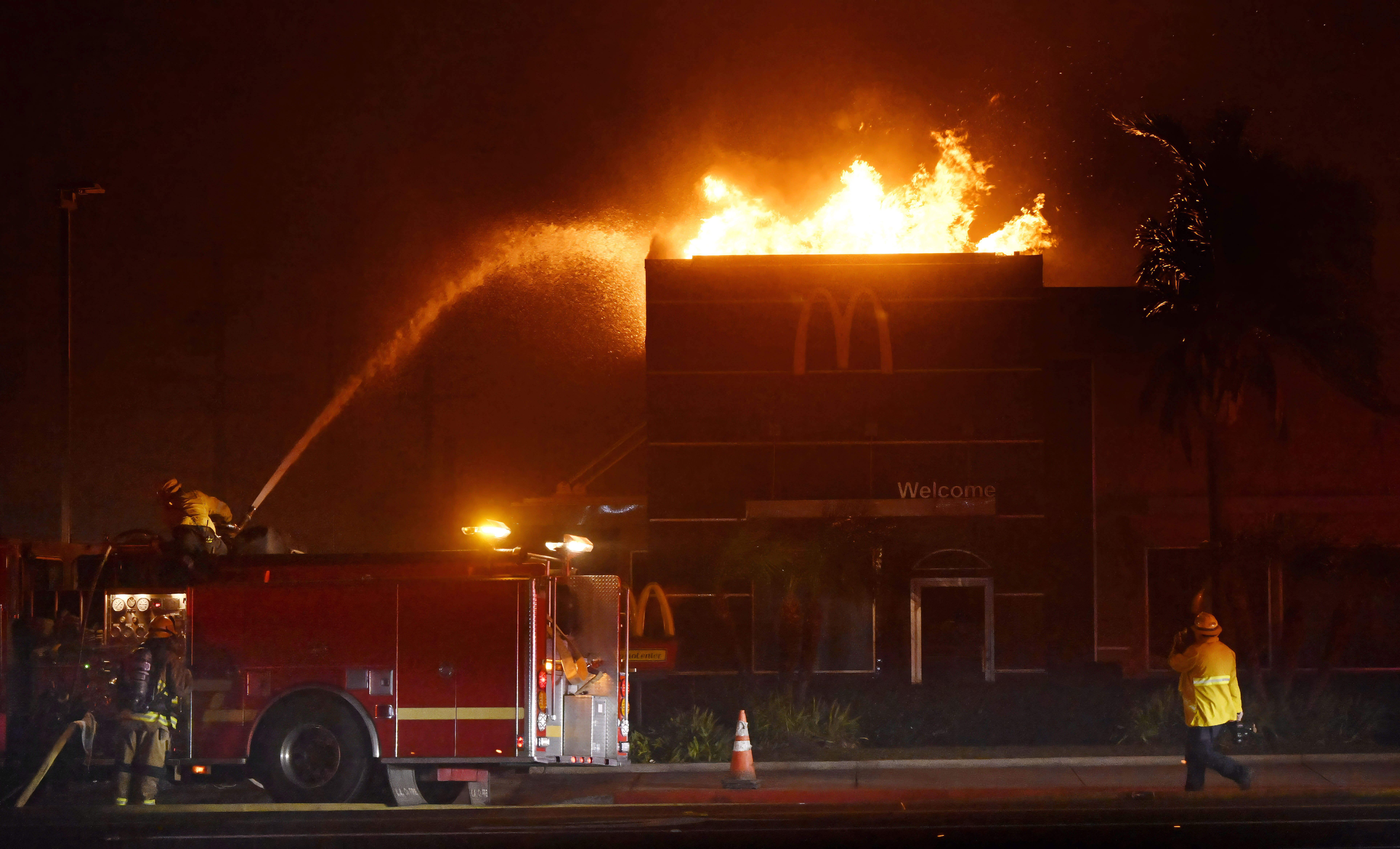 Firefighters try to extinguish the flames as a McDonald’s burns...