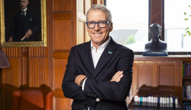 Pres. Milliken in a suit leaning against a desk