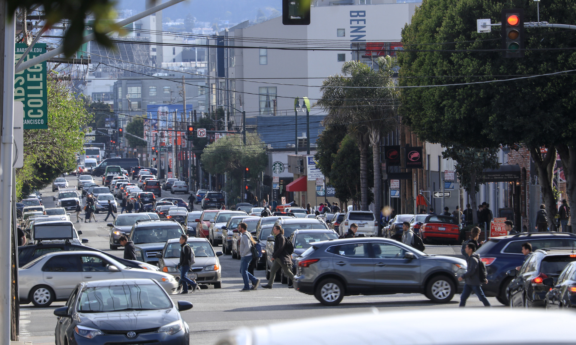 Several cars are on the road along with people crossing the street.