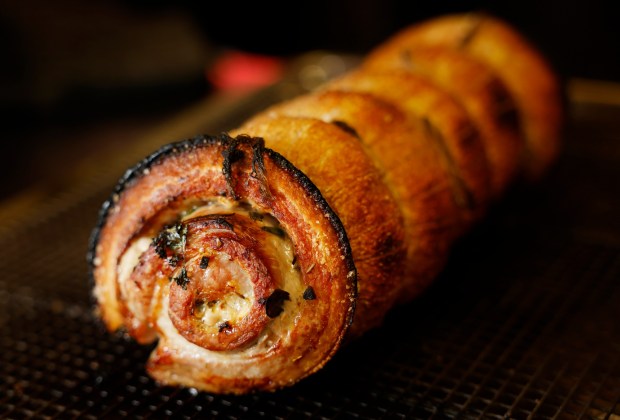 A pork belly is butterflied, seasoned, tied and slow-roasted by chef Sid Hilarides, then the outside is crisped during the process to produce a versatile porchetta at Allmine in Oceanside. (K.C. Alfred / The San Diego Union-Tribune)