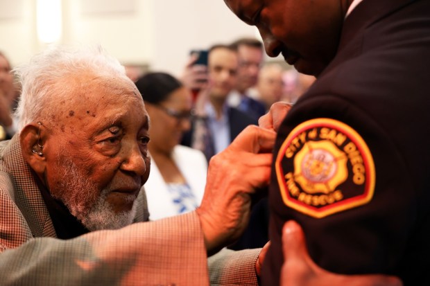 Ben Holman pins the badge onto the chest of San Diego Fire Chief Robert Logan during his swearing-in ceremony in August 2024. (Aryka Randall)