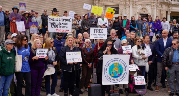 SAN DIEGO, CA - JANUARY 24: Surrounded by concerned citizens, Margaret Virissimo, a founding member of San Diego United Communities, speaks during a rally at the Organ Pavilion in Balboa Park, protesting the newly implemented parking fees at the park, Saturday January 24, 2026, in San Diego, California. (Howard Lipin / For The San Diego Union-Tribune)