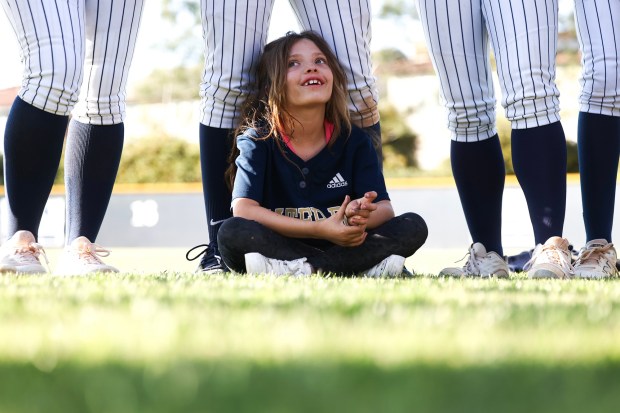 McKenna Cooney, 7, sits on the cleats of Mater Dei's Charlize Masingale after the Crusaders beat Christian at Mater Dei Catholic High School on Tuesday, April 8, 2025 in Chula Vista, CA. Cooney, who was born deaf, is the team's honorary player. (Meg McLaughlin / The San Diego Union-Tribune)