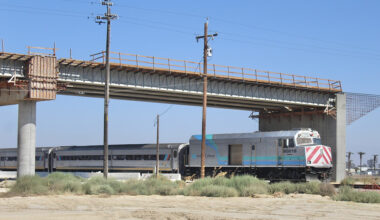 Passenger train travels beneath bridge under construction.