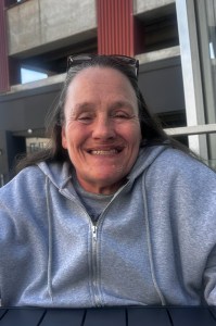 A person in a zippered hoodie, with sunglasses on their head, smiling