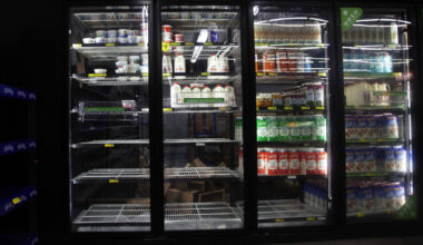 Glass-door refrigerator at a grocery store with mostly empty shelves, displaying limited dairy and juice products.