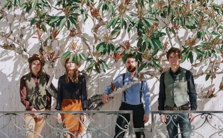 Musicians standing amid the low-hanging branches of a flowering tree.
