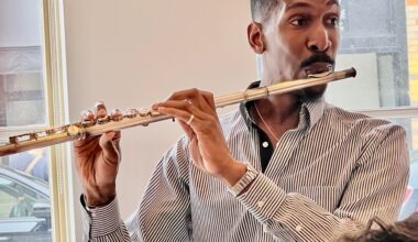 A person in a striped shirt plays the flute indoors near a window.