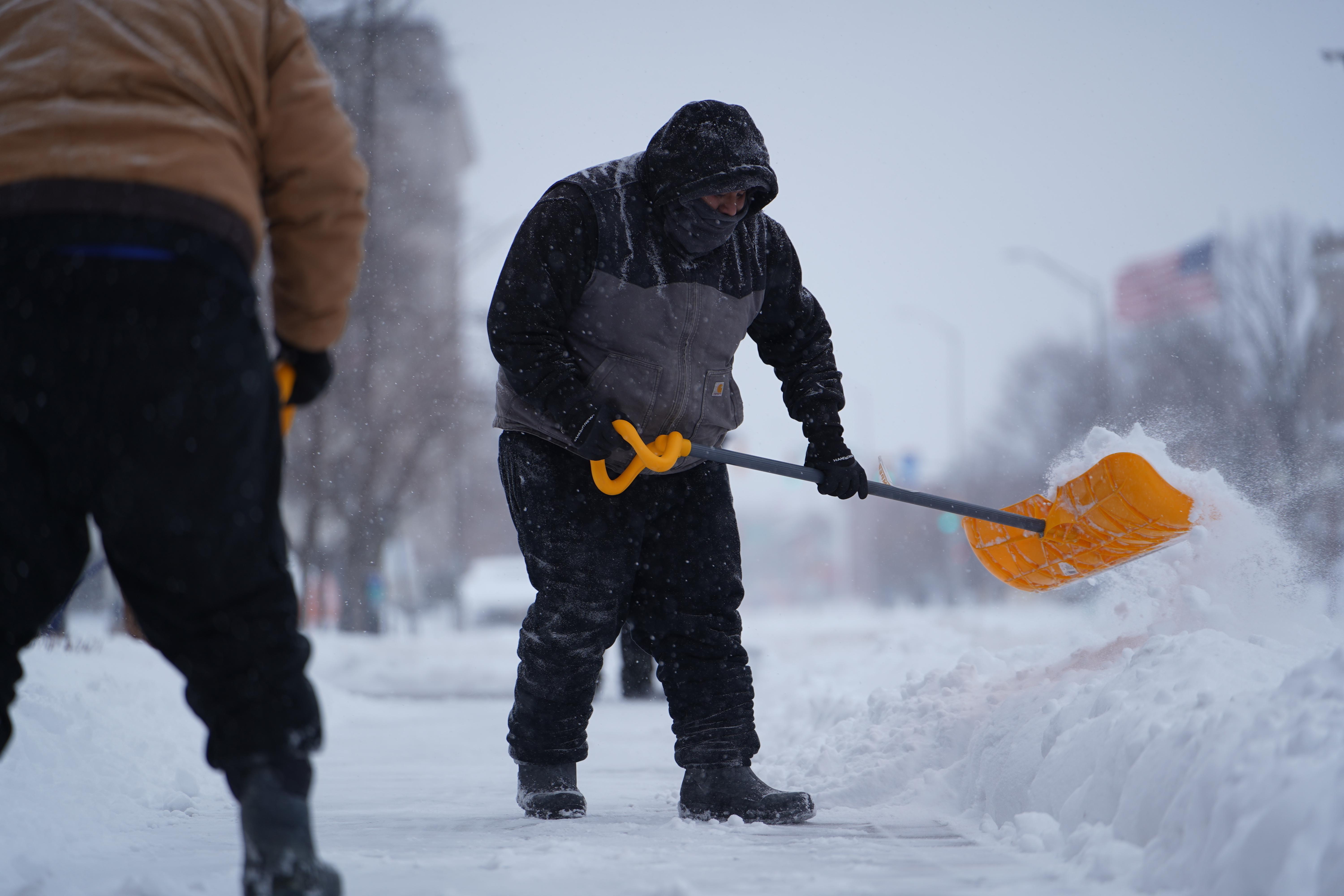 Workers shovel snow from a sidewalk in downtown Indianapolis, on...