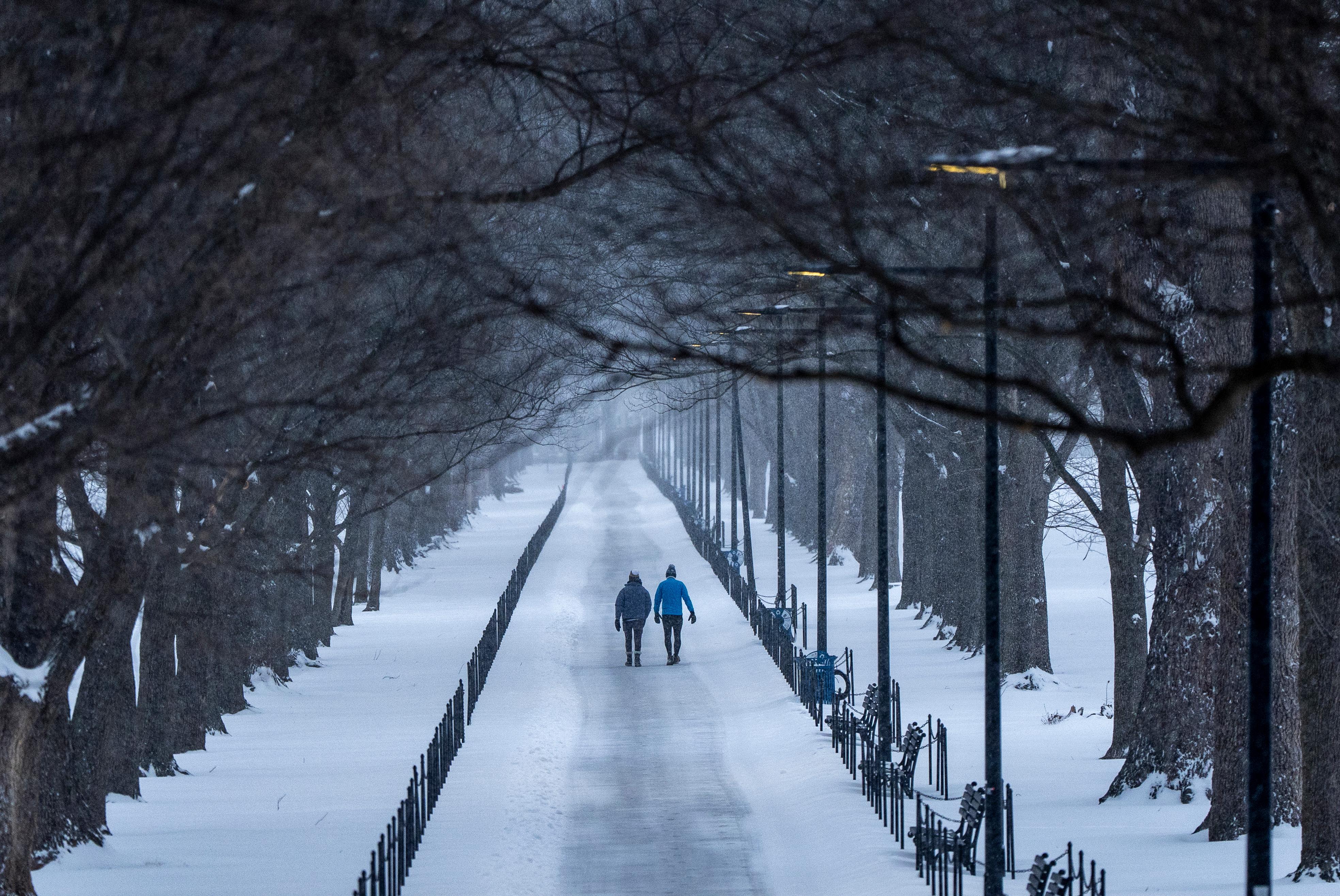 Two people walk along the National Mall as snow falls,...
