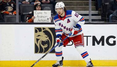 Artemi Panarin, wearing a white New York Rangers away jersey with a blue 'A', is on the ice with his stick during a game. In the background, a fan holds a sign that reads, "Come to Anaheim Artemi!".