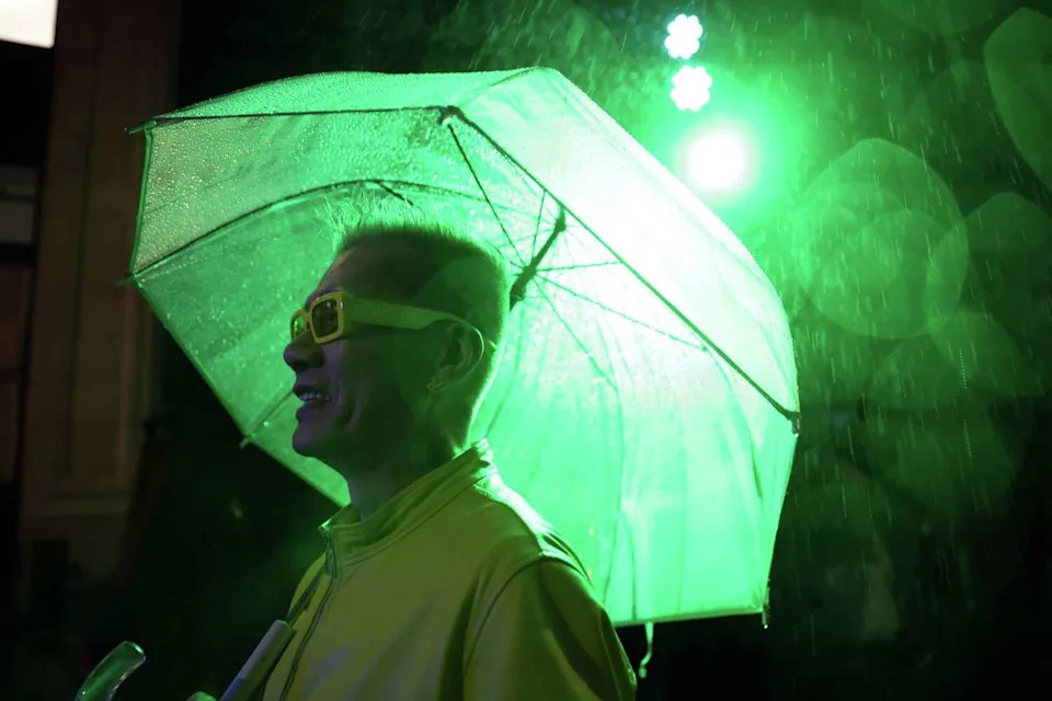 As rain falls, Benjamin Tan watches as Magnolia Polaris & Booty Juice B2B performs on Jesse Street west of 2nd Street during a Downtown First Thursdays street party in San Francisco on Thursday. (Scott Strazzante/S.F. Chronicle)