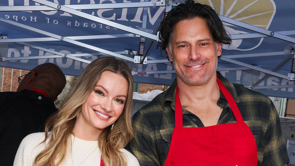 Caitlin O'Connor wearing a white sweater standing next to Joe Manganiello wearing a plaid shirt and a red apron.