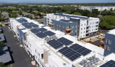 Aerial view of a California apartment complex with large rooftop solar arrays covering multiple flat buildings.