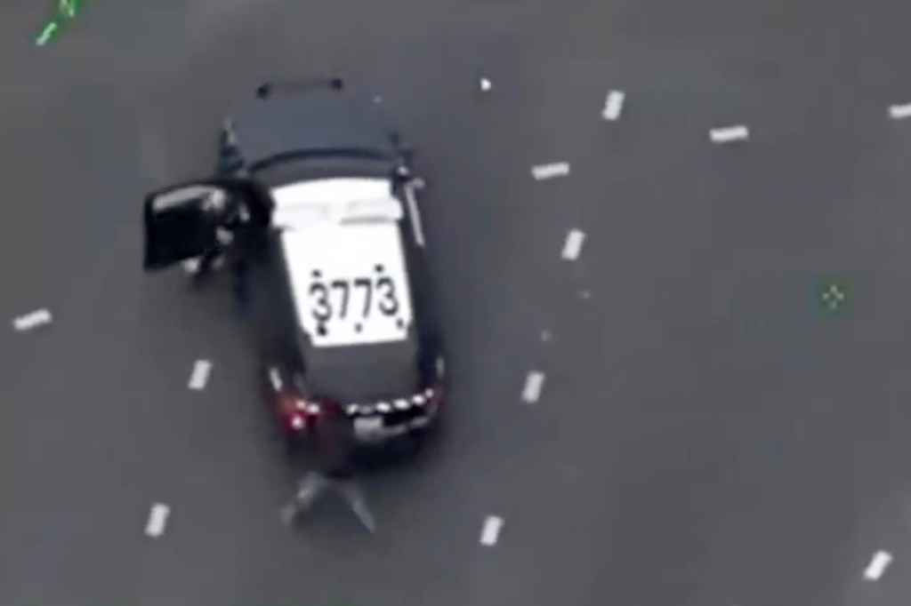 An overhead view of a police car with an open door and a person on the ground next to it.