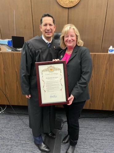 Israel Claustro and Katrina Foley holding a framed document in a courtroom.