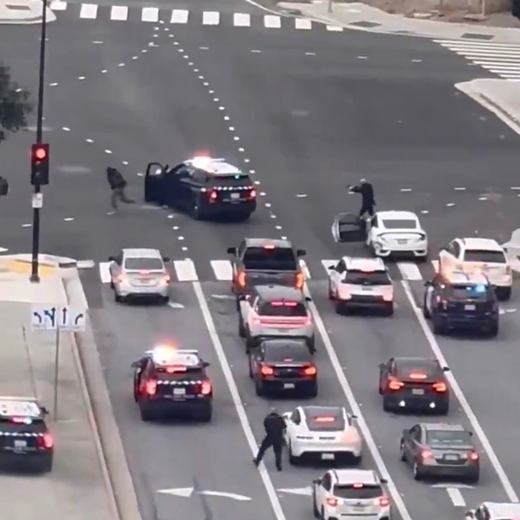 An aerial view of a busy street with several police vehicles and officers on foot, seemingly involved in a shootout or chase.