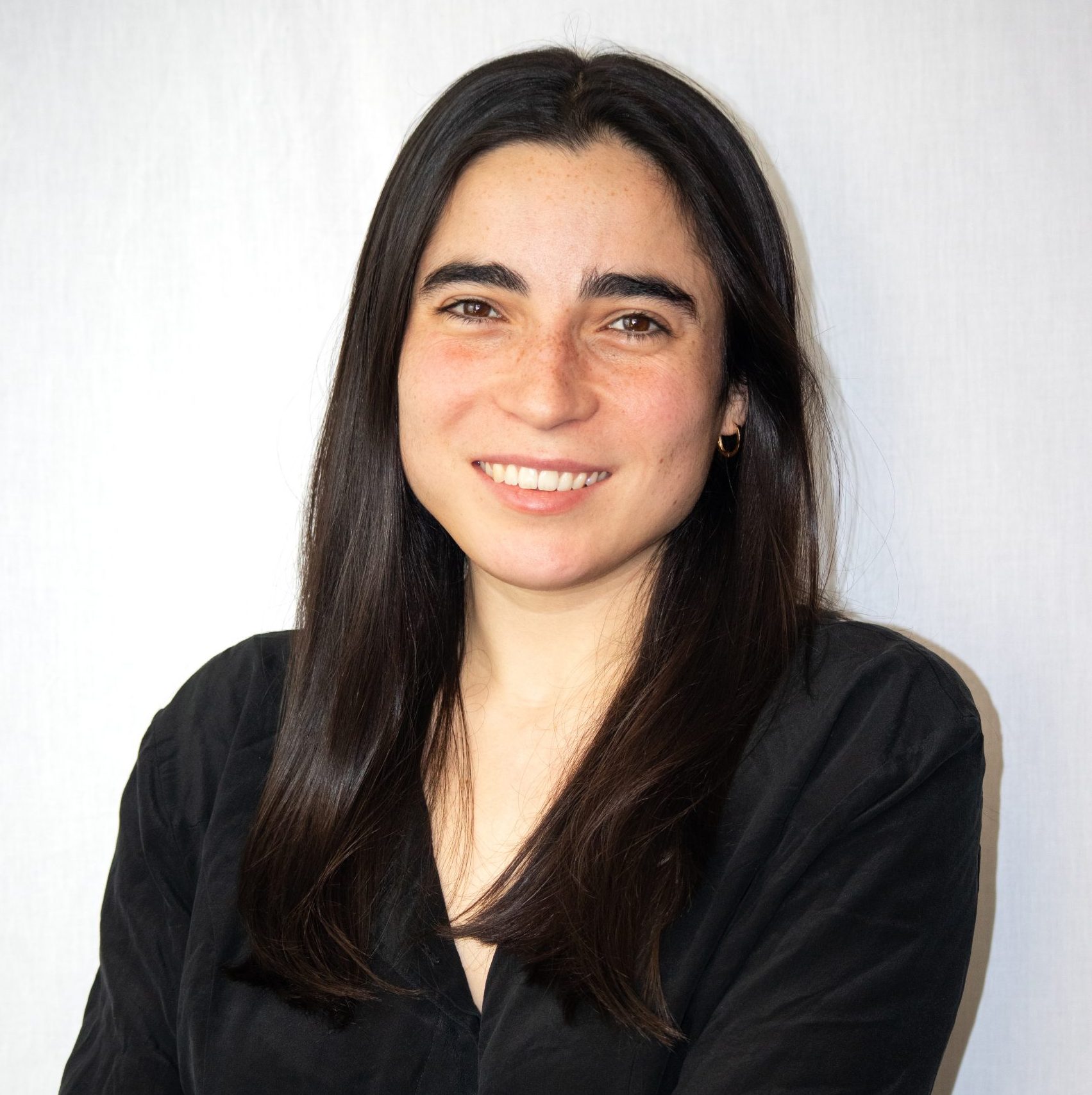 A woman with long dark hair and a black shirt smiles at the camera against a plain light background.