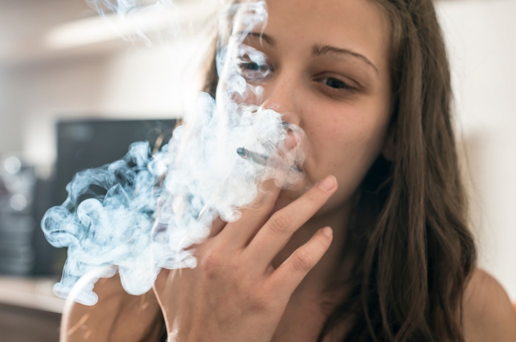 Close-up of a young woman with long hair smoking a cigarette indoors.