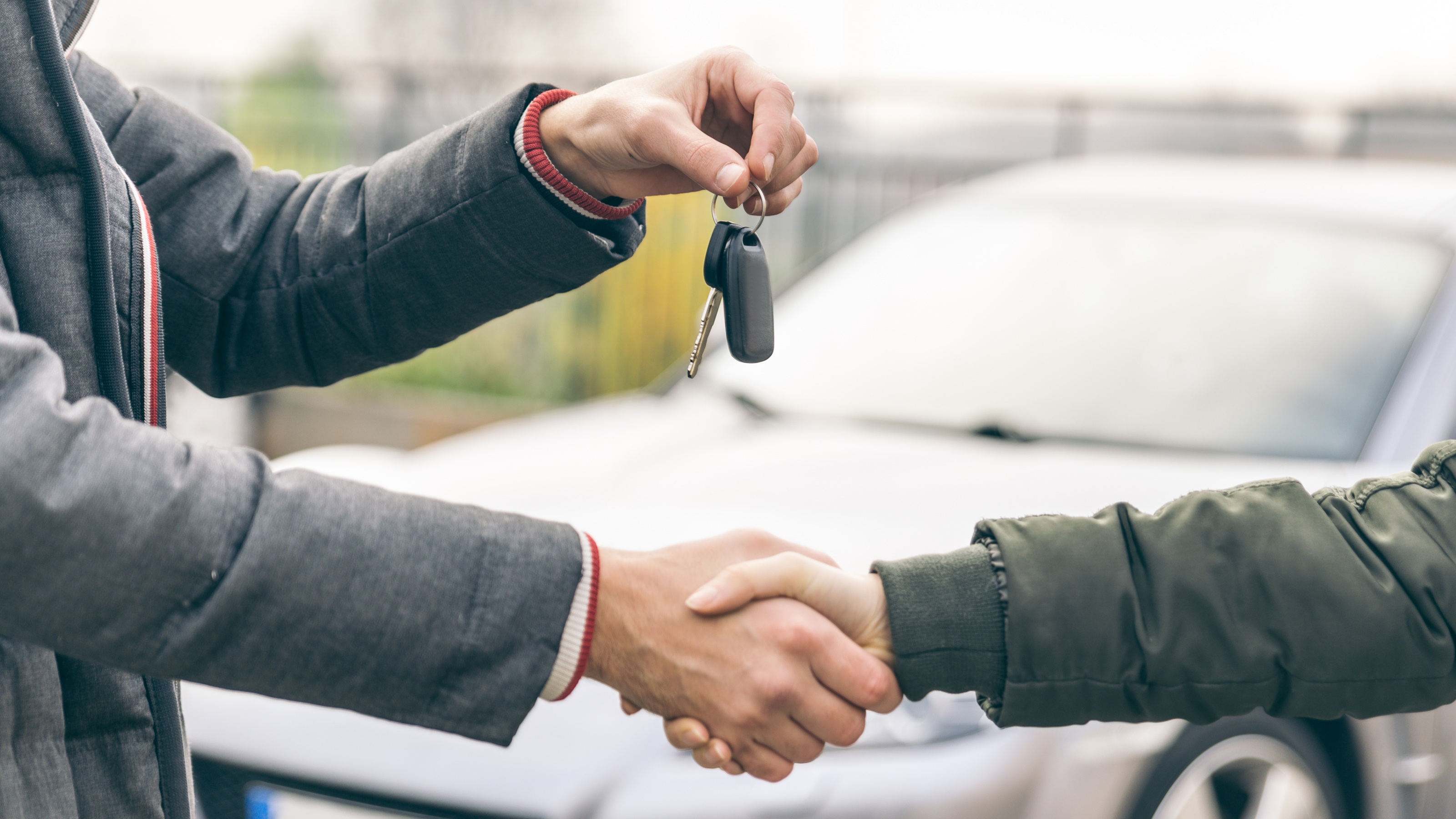 A man holds up keys to a new car while shaking the buyer's hand.
