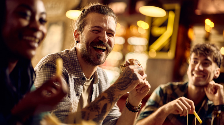 A man eats a burger with friends in a bar