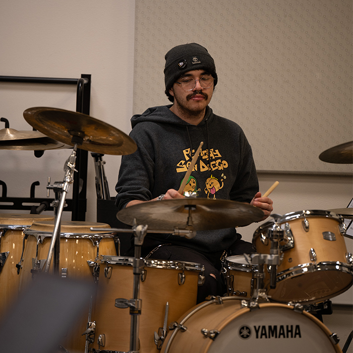 male student wearing a beanie sitting at a drum set