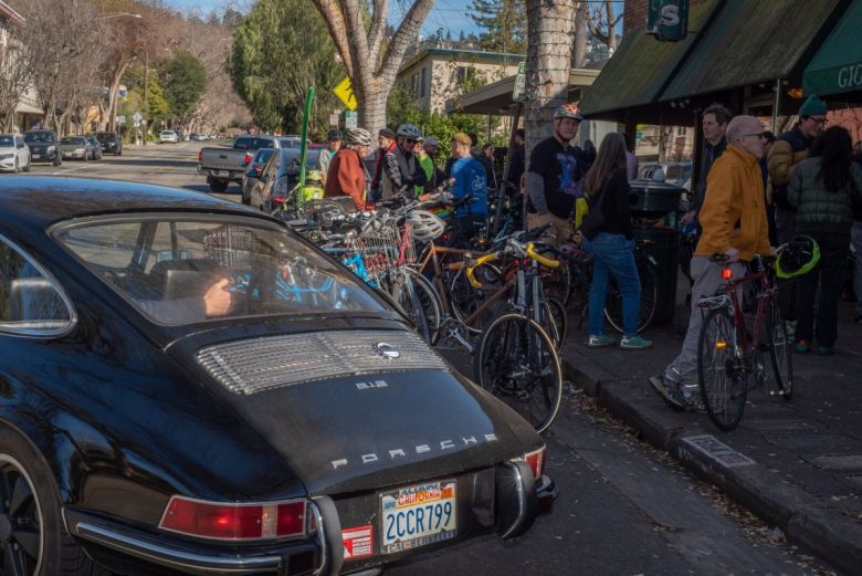 A driver backs into a parking space in front of the shops on Hopkins Street, where dozens of bicyclists are taking part in a rally.