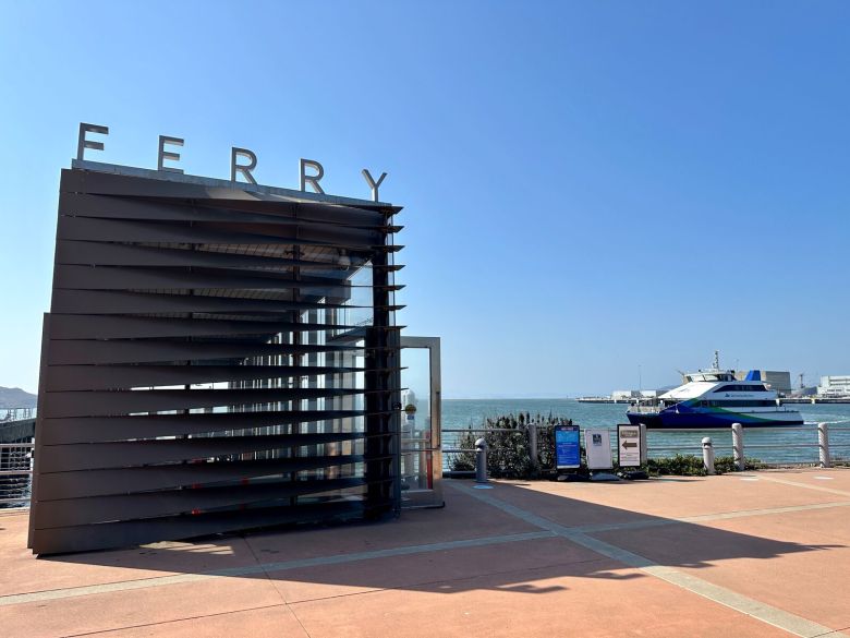 A view of a pier with a sign that says "ferry" and a white ferry boat on the water behind it