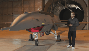 A man stands next to a large, gray unmanned aerial vehicle (UAV) in a hangar.