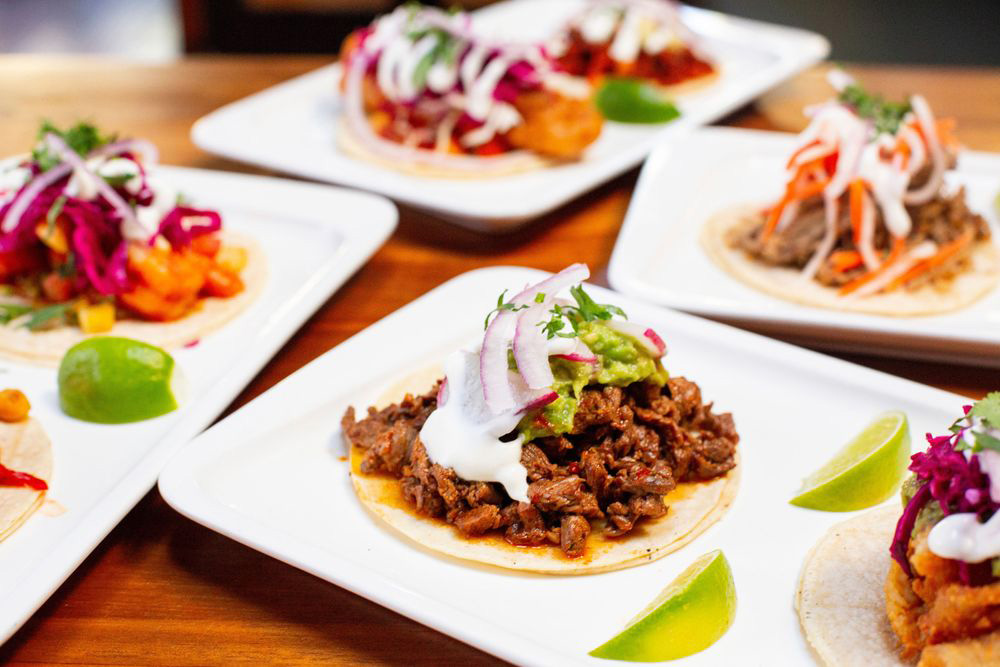 Several white plate with tacos on a wooden table.