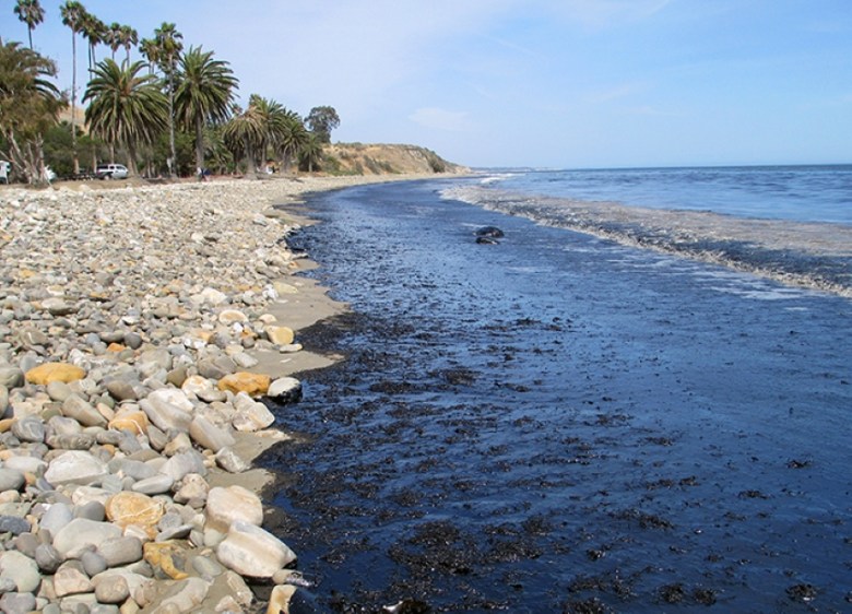 Rocky beach with oil pollution on the sand and ocean.