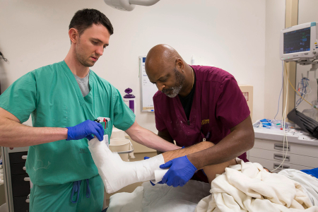 Two medical staff members work together to apply and secure a cast on a patient’s lower leg.