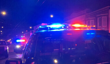 Police vehicles with flashing lights are parked on a dimly lit street at night.