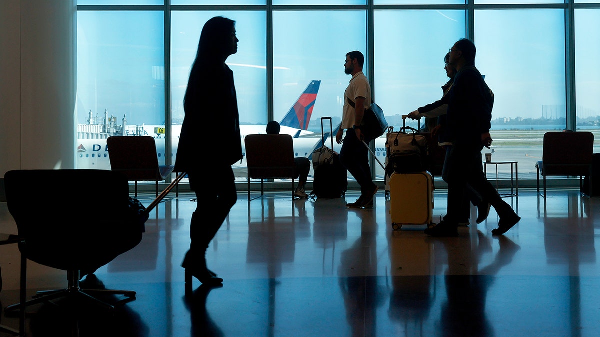 Travelers walking through San Francisco International Airport terminal with large windows, silhouettes, and an airplane visible outside.