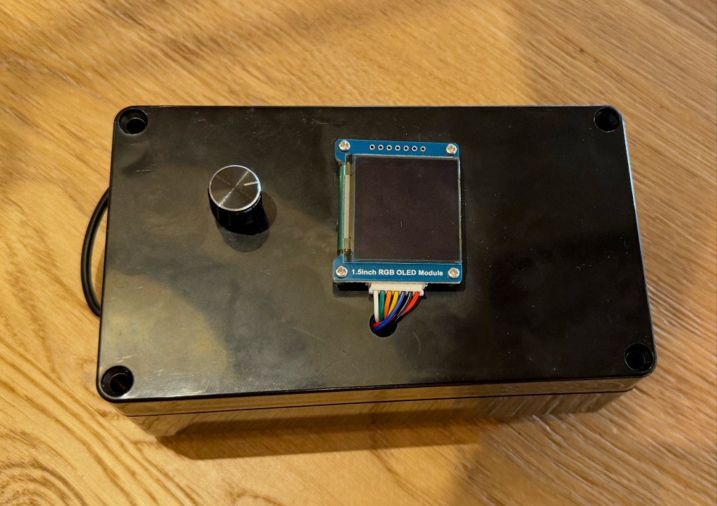 A black rectangular box with a silver knob, a multi-colored wire and a 1.5-inch RGB OLED module.
