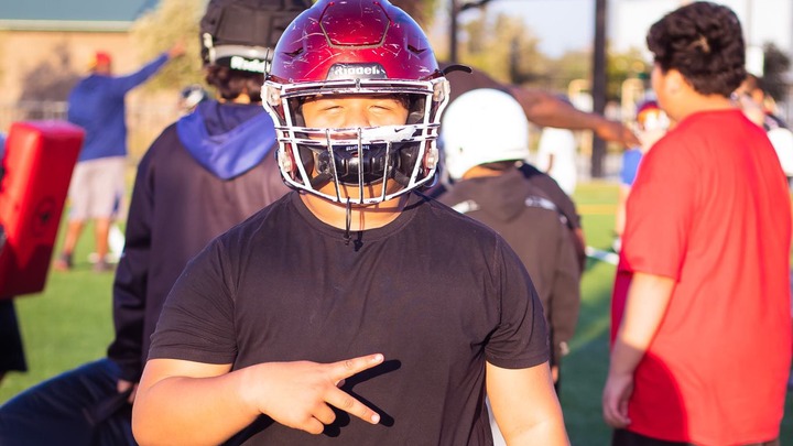 Jeremy Rosales wearing a maroon football helmet, making a peace sign with his left hand.