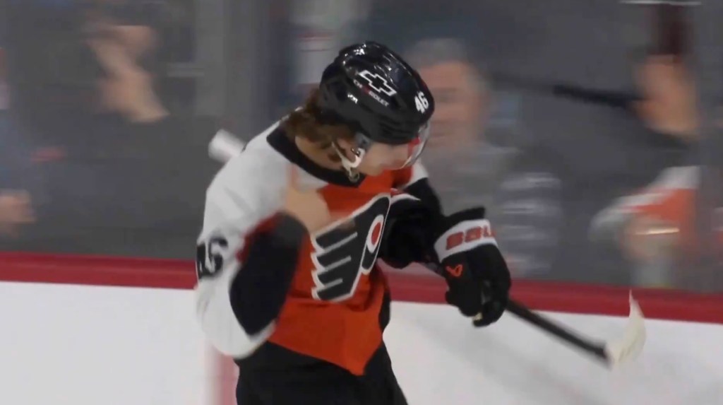 Trevor Zegras giving a thumbs up in a Philadelphia Flyers jersey and hockey helmet, holding a hockey stick.