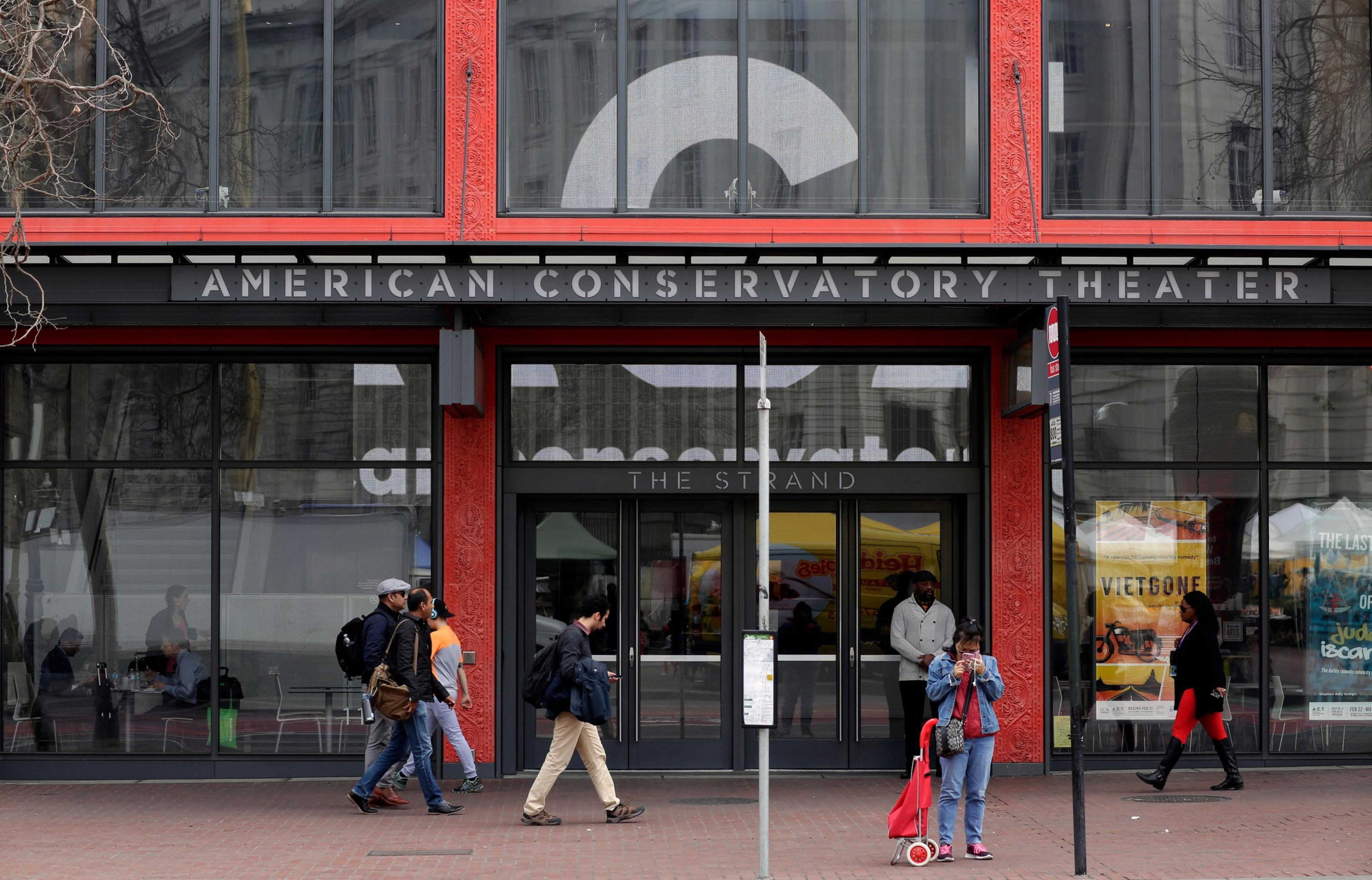 A red and black theater entrance labeled “American Conservatory Theater” with several people walking or standing outside on a city sidewalk.