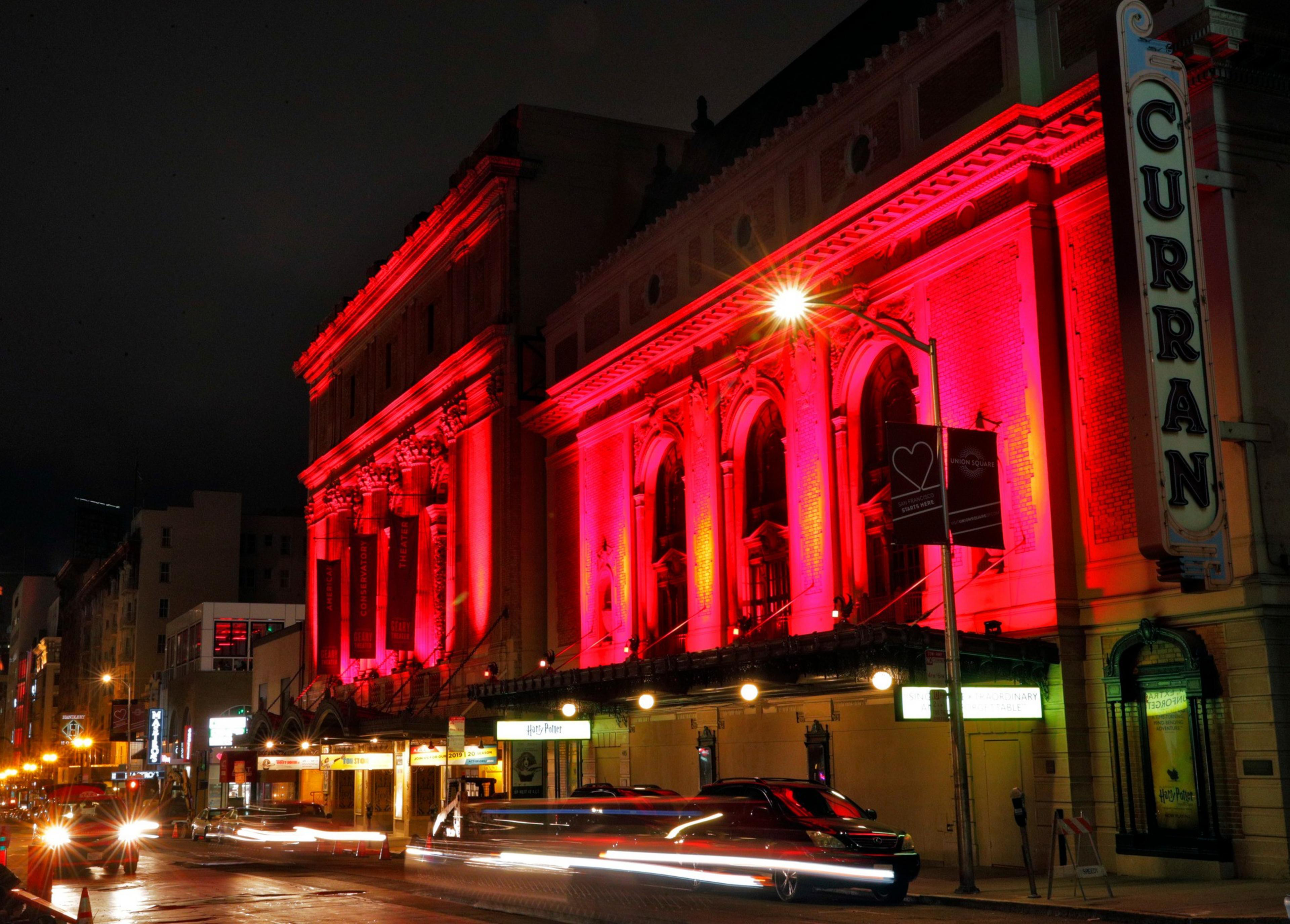 A historic theater building lit with vibrant red lights at night, with a vertical sign reading “CURRAN” and busy street traffic in front.