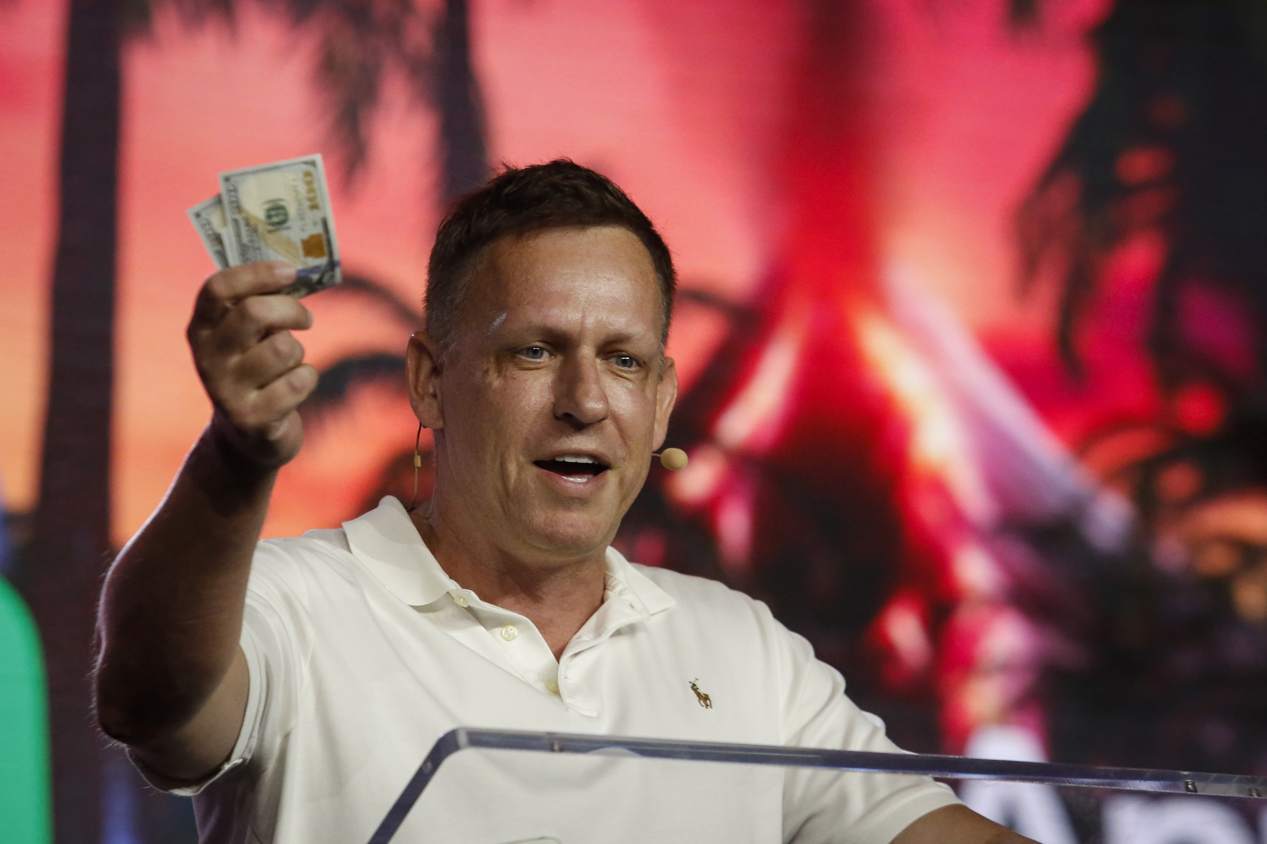 Peter Thiel holding hundred dollar bills while speaking at the Bitcoin 2022 Conference.