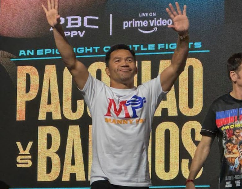 A man in a T-shirt raises his arms in front of banner that reads "Pacquiao vs. Barrios."