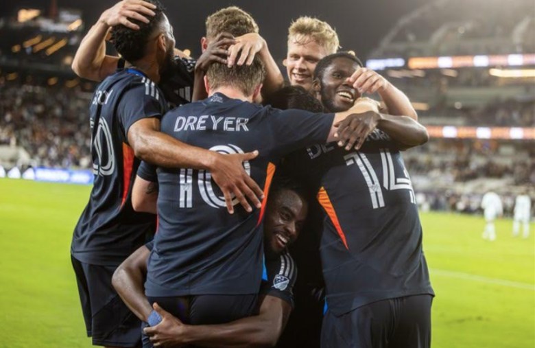 A group of men embrace on the soccer pitch. The jersey on the man in the center readers "Dreyer" with the number 10.