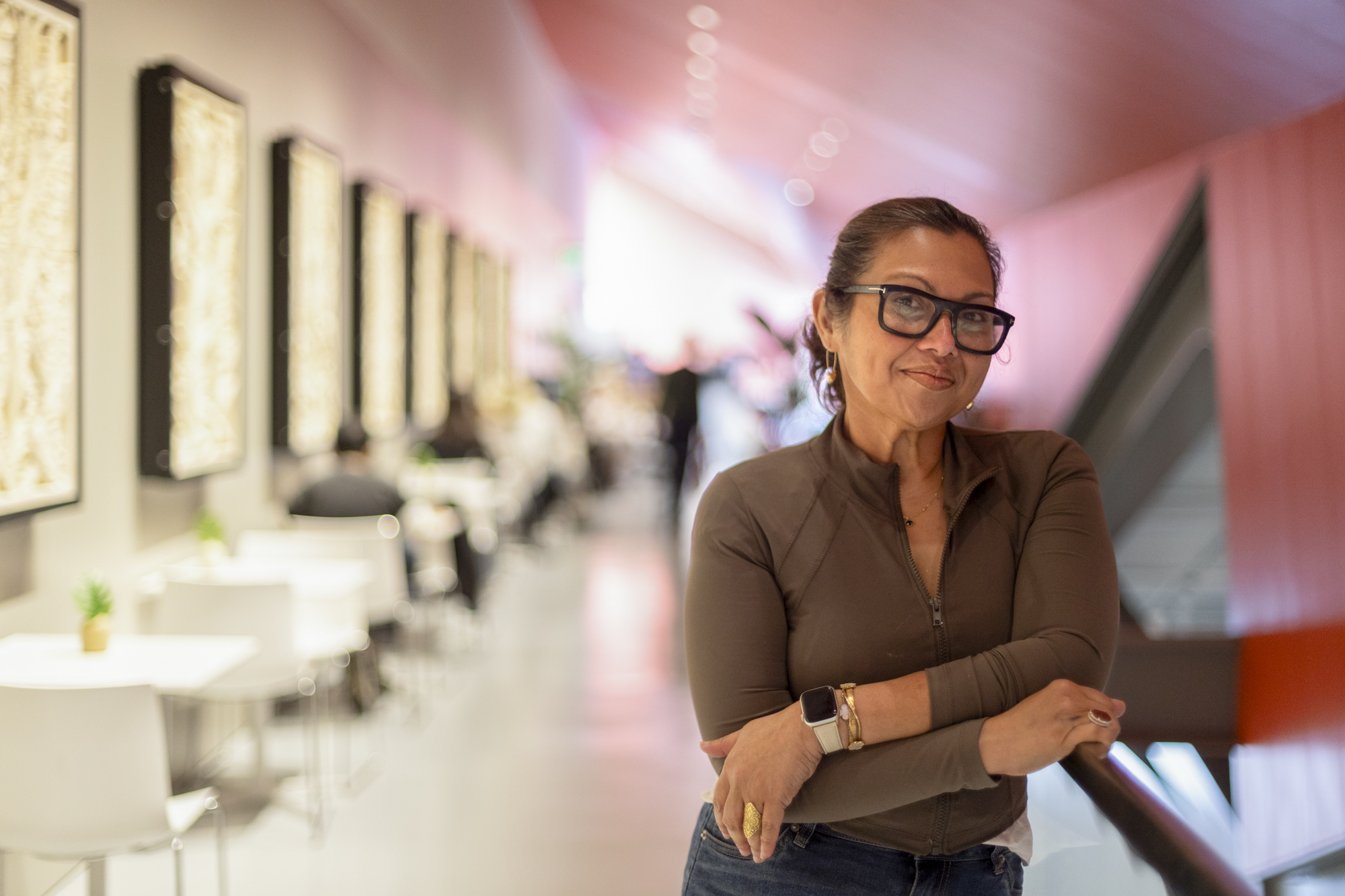A woman in glasses poses inside a cafe.