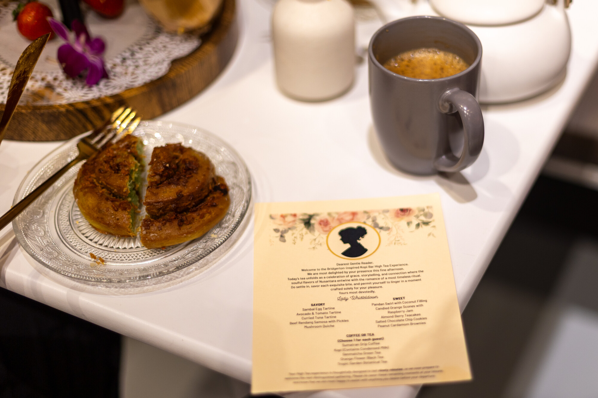 Close-up on a pandan pastry, a cup of tea and a menu for a special high tea event.